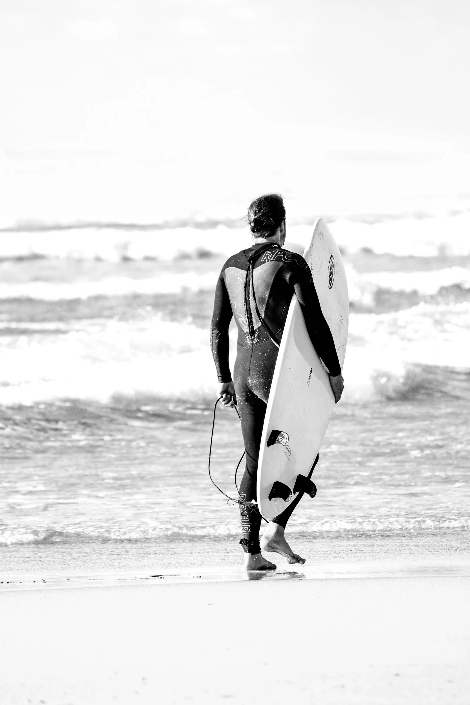 Un surfeur en combinaison porte sa planche face à l’océan