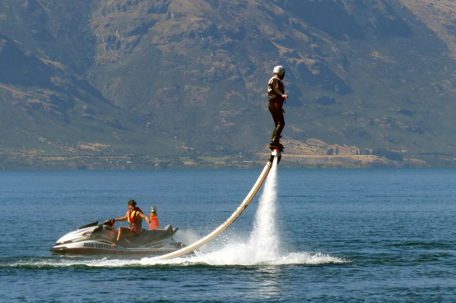 Une personne portée au-dessus de l’eau par les jets d’un flyboard relié à une motomarine