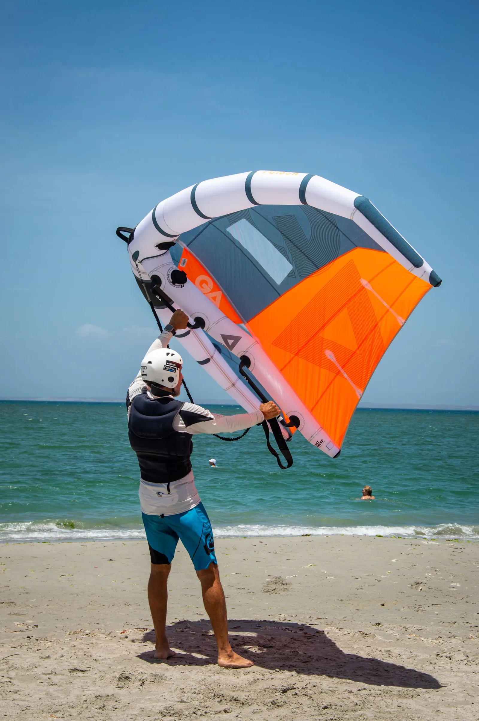 Un pratiquant casqué tient une aile de wing sur la plage