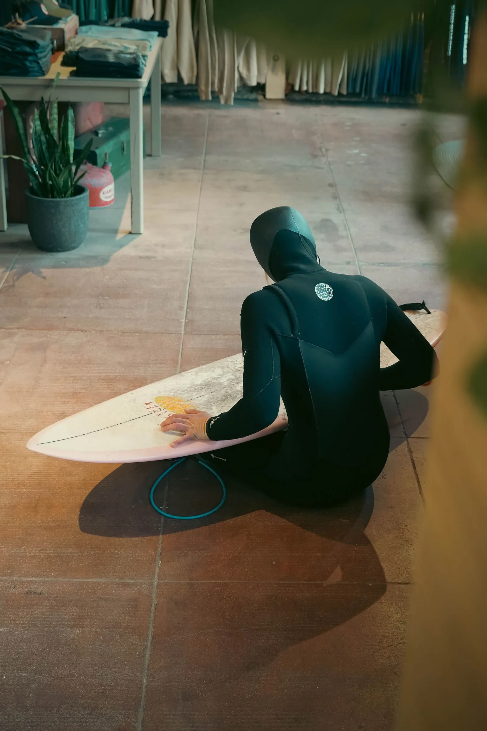 Une surfeuse en combinaison prépare sa planche à l’intérieur